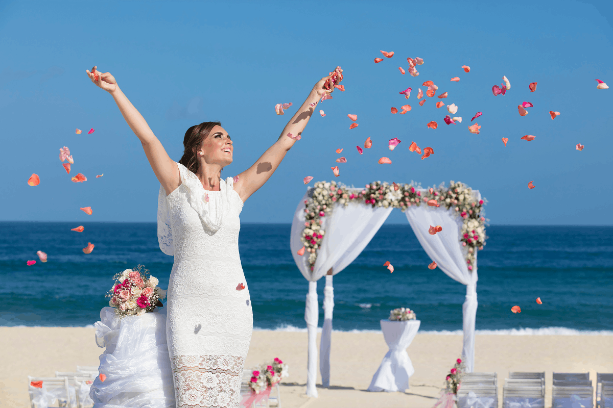 Novia celebrando su boda en la playa de Krystal Grand Los Cabos con pétalos, altar floral y vista al mar.